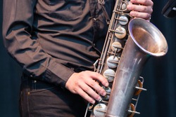 Close up view of the hands of a male saxophonist playing a tenor saxophone in an orchestra, a reed woodwind instrument popular in jazz, classical and blues music