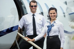Portrait of happy confident airhostess and pilot standing on private jet's ladder