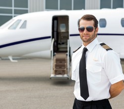 Portrait of confident pilot wearing sunglasses with private jet in background