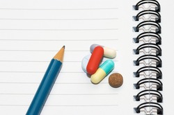 Empty blank ring, notepad, one pencil on white page with pills to indicate relation with pharmaceutical industry, or metaphor for office/school stress or work-related drug research