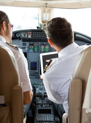 Rear view of pilot and copilot using digital tablet in cockpit of private jet