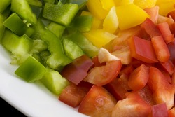 diced green, red and yellow bell pepper on a white plate ready for cooking or salad