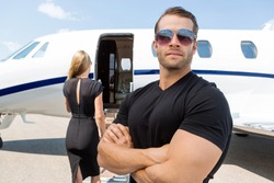 Confident bodyguard wearing sunglasses while standing against woman and private jet