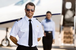 Portrait of confident pilot standing with stewardess and private jet in background at terminal