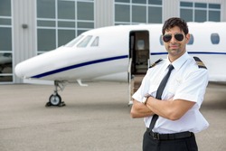 Portrait of handsome pilot with arms crossed standing in front of private jet