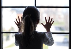 Young girl at window (in partial silhouette) hands pressed against window, pensive or wanting out?