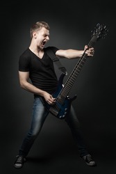 young male musician playing a six-string bass guitar isolated on dark background
