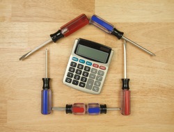 House Shaped by Screwdrivers and Calculator on a Wood Background.
