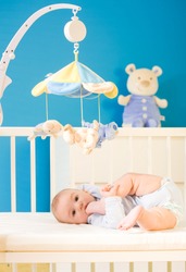 Infant baby resting and playing in his little baby bed at nursery. Toys are officially property released.