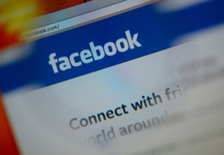 LISBON, PORTUGAL - AUGUST 3, 2014: Photo of Facebook homepage on a monitor screen through a magnifying glass.