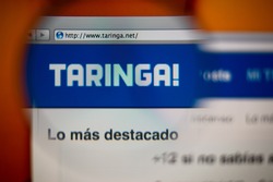 LISBON, PORTUGAL - AUGUST 27, 2014: Photo of Taringa! homepage on a monitor screen through a magnifying glass.