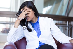 Closeup portrait, young depressed woman healthcare practitioner holding face in despair, isolated hospital background
