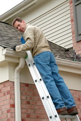 Roof Repair - Man on a ladder, cleaning the gutters and repairing the roof shingles.