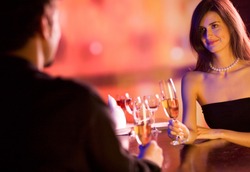 Young couple sharing champagne glasses in restaurant, celebrating or on romantic date. Focus on woman.