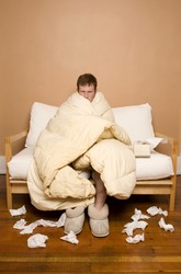 A man sick with the flu/cold peeking out from under his blanket