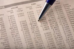 Close-up of currency exchange rate section of a financial newspaper, with pen pointing at forex rates
