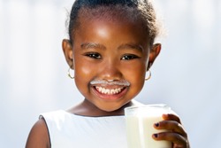 Close up fun portrait of cute African girl showing white milk mustache.Isolated against light background.