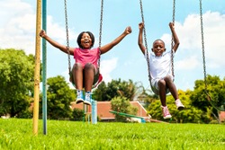 Action portrait of shouting African kids playing on swing in neighborhood.Out of focus houses in background.