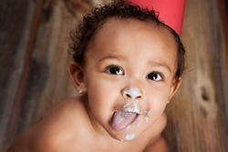 Close up of an adorable baby boy with cake icing all over his face and his tongue sticking out.