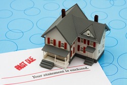 Grey model house with past due bills sitting on a blue background, foreclosure