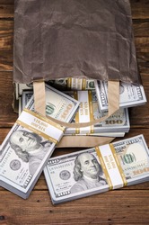 Brown paper bag containing that moolah. Bag full of money - vintage photography of brown paper bag with stacks of hundred dollar bills on wooden background