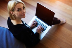 Lovely young woman working on laptop computer at home, attractive blonde hair student using laptop in her living room and look to the camera, female freelancer working at home