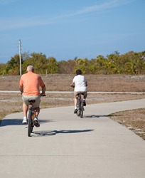 Rear view of a senior couple riding their bicycles. Focus on the husband, in the foreground.