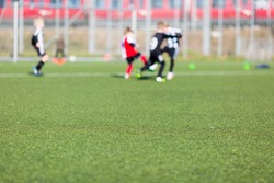 Blur of young kids playing a soccer training match outdoors on an artificial soccer pitch.