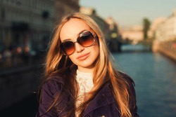 beautiful blonde girl in sunglasses posing on the street near the river in the violet cloak