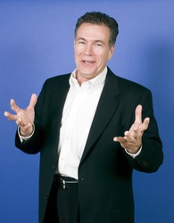 Handsome, mature, white male wearing a black suite and a white shirt gesturing happily as if telling a joke or funny story.