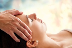 Close up head portrait of young woman having facial massage in spa. Therapist doing head massage against colorful background.