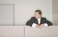 Businessman looks down from his cubicle in his office while wearing a black suit and gold tie