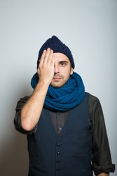young business man closes one eye, hand, winter style clothes, studio shot isolated on the gray background
