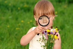 Cute little girl looking at bouquet of field flowers through magnifying glass