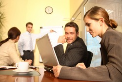 A business team of two men and two women work together with a laptop and a flip chart in a conference room to prepare a new business proposal for a client.