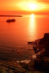 Image shows one of the famous sunsets in Santorini, greece, while a cruise ship is traveling towards the open sea
