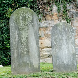 Two ancient headstones in a cemetery. The aging of the stone has worn away any words that may have once been present.