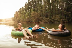 Portrait of happy young friends in inflatable rings floating on lake. Young people relaxing in water on a summer day. Enjoying their holidays at the lake.
