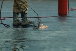 Installation of roll roofing waterproofing propane blowtorch during construction