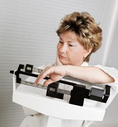 Mature woman looks disappointed at her progress losing weight, on weight scale.