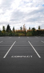 Vertical photograph of a parking lot with the word COMPACT in all spaces with trees and sky in background.