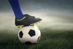 Portrait of football player ready to kick the ball at field under cloudy sky