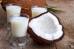 Coconut milk in a glass with coconut shells on old wooden background,selective focus