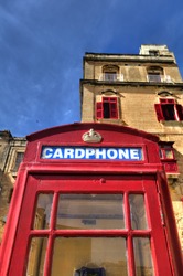 An old red cardphone booth in the historic city Valletta with an old apartment building in the background