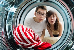 Funny couple loading clothes to washing machine. From inside the washing machine view.