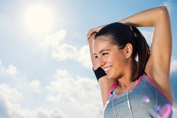 Close up face shot of attractive young runner getting ready for morning run.Woman with charming smile stretching arms and neck against sunny sky.