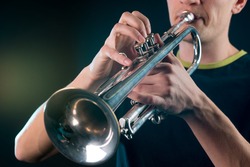 Hard process of playing the vintage trumpet with the man blowing out the air into the tube and meanwhile pressing the buttons of the musical instrument.