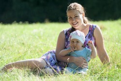 Young mother and her little baby are on green grass. They are smiling. Summer time. Sunny