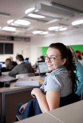 young pretty female college student sitting in a classroom full of students during class