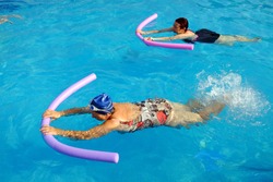 Top view of two senior women doing swimming exercise with soft foam noodles in outdoor swimming pool.